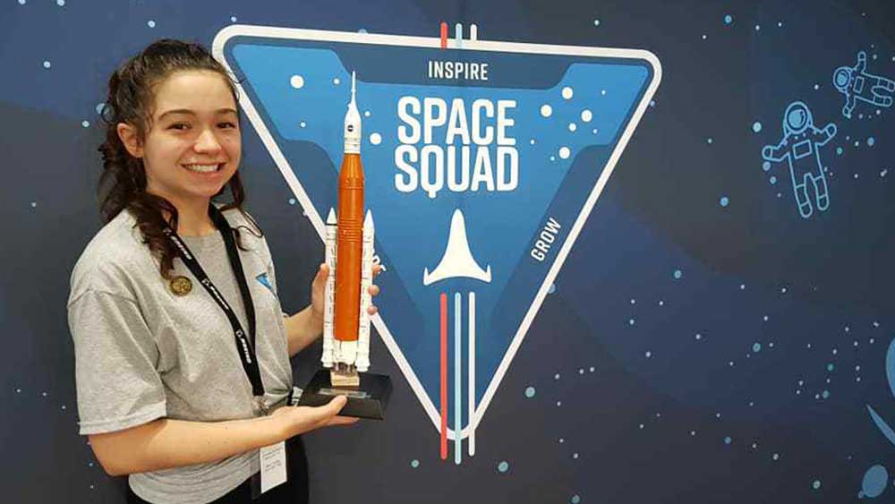 Young student holding a model of the Space Launch System in front of a Space Squad logo